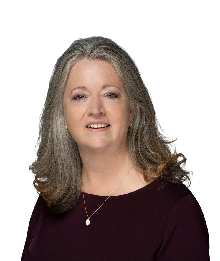 A woman with long, wavy gray hair wearing a dark top and a gold necklace with a pearl pendant, smiling at the camera against a white background.